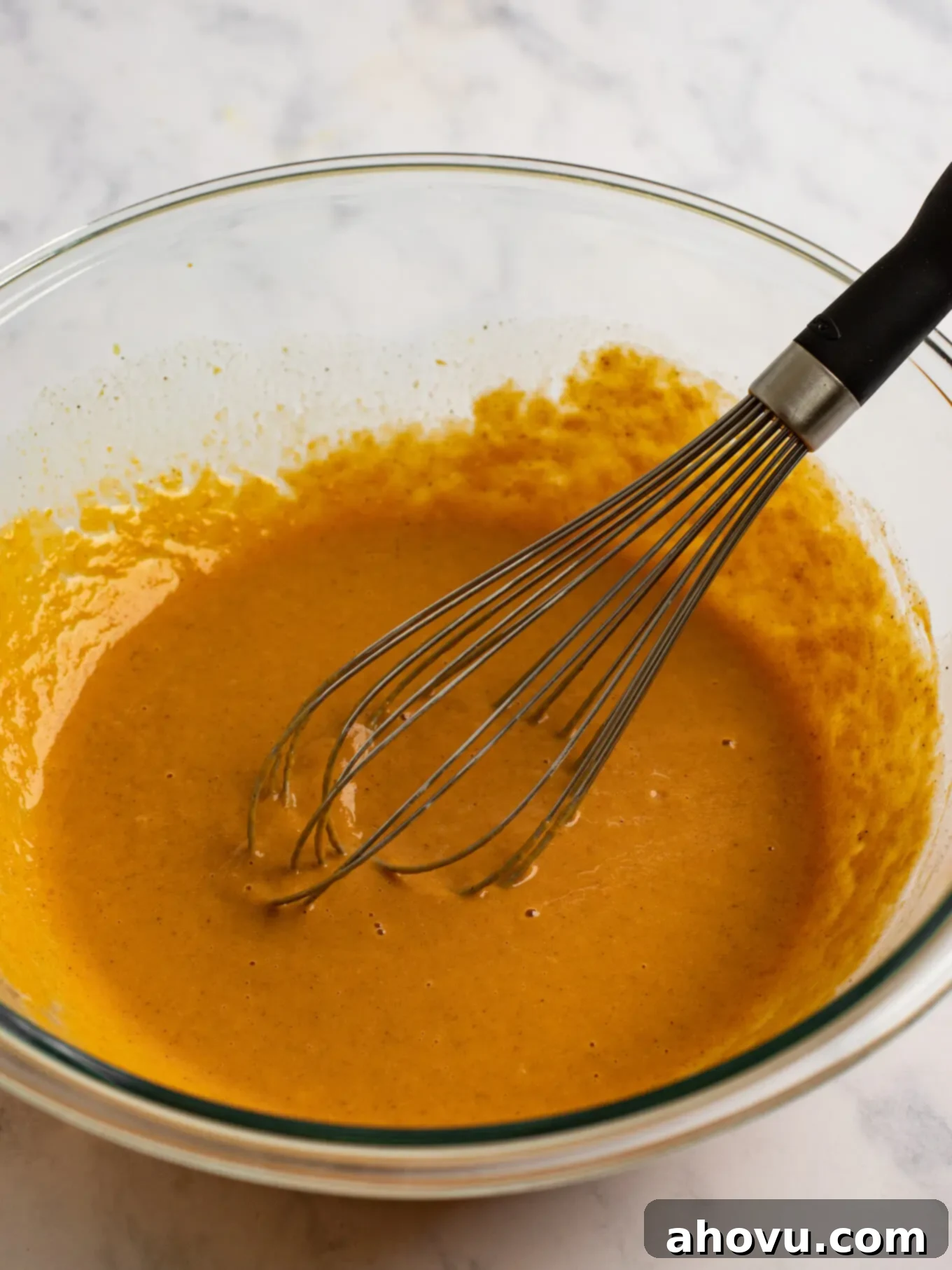 The filling ingredients whisked together in a glass mixing bowl. A whisk rests on the side of the bowl.