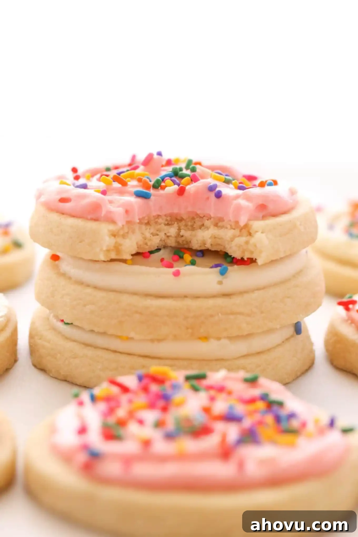 A stack of three soft cut out sugar cookies topped with frosting. Additional cookies surround the stack. 