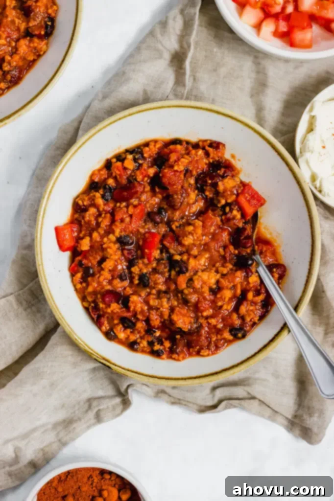 A bowl of turkey chili with a spoon in it. Several bowls with sour cream, diced tomatoes, and more chili are around it.