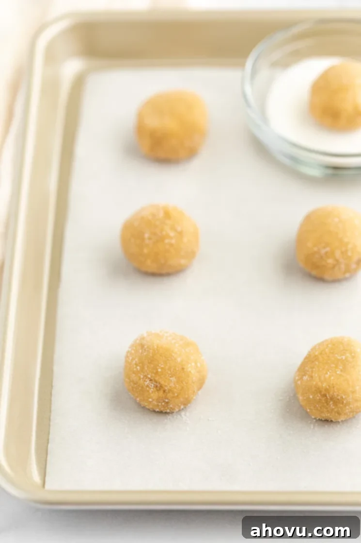 Grandma's Peanut Butter Blossoms 4 A baking sheet lined with parchment paper and cookie dough balls covered in sugar on the pan.