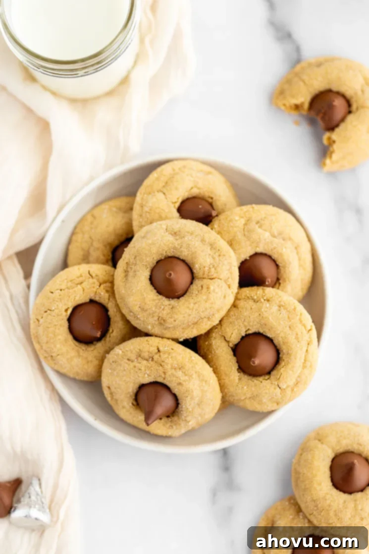 Grandma's Peanut Butter Blossoms 6 A plate with several peanut butter blossom cookies stacked on it with a glass of milk and a cookie with a bite taken out of it in the background.
