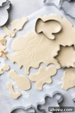 Freshly rolled cookie dough, perfectly cut into various festive shapes on parchment paper, awaiting baking.