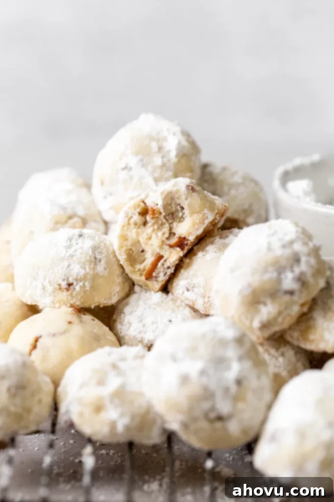 Easy Snowball Cookies Video 2 A pile of freshly baked snowball cookies on a cooling rack, with one cookie playfully showing a bite taken out of it, revealing its delicious shortbread interior.