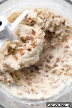 A glass mixing bowl filled with creamy, light-colored cookie dough, textured with finely chopped pecans, ready for shaping.