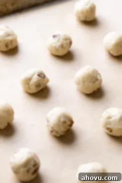 A baking sheet lined with parchment paper, holding neat rows of unbaked, perfectly rounded balls of snowball cookie dough, ready for the oven.