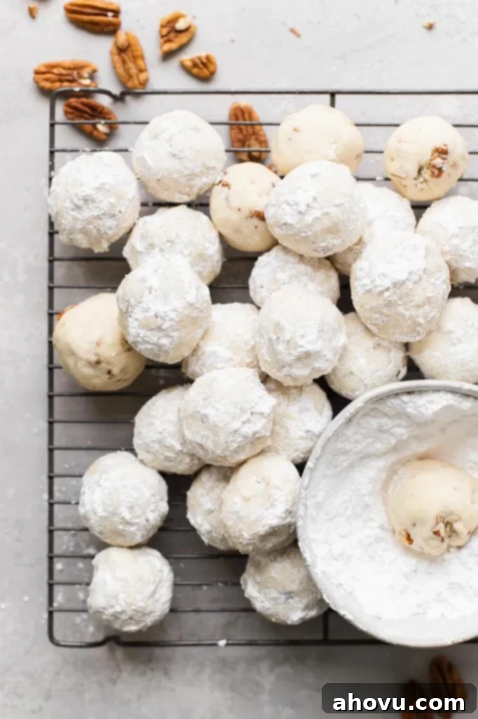Easy Snowball Cookies Video 5 A wire cooling rack brimming with a fresh batch of beautiful snowball cookies, all perfectly coated in a generous dusting of powdered sugar, ready to be enjoyed.