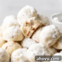 Easy Snowball Cookies Video 6 A freshly baked batch of delightful snowball cookies, perfectly round and generously coated in powdered sugar, resting on a cooling rack.