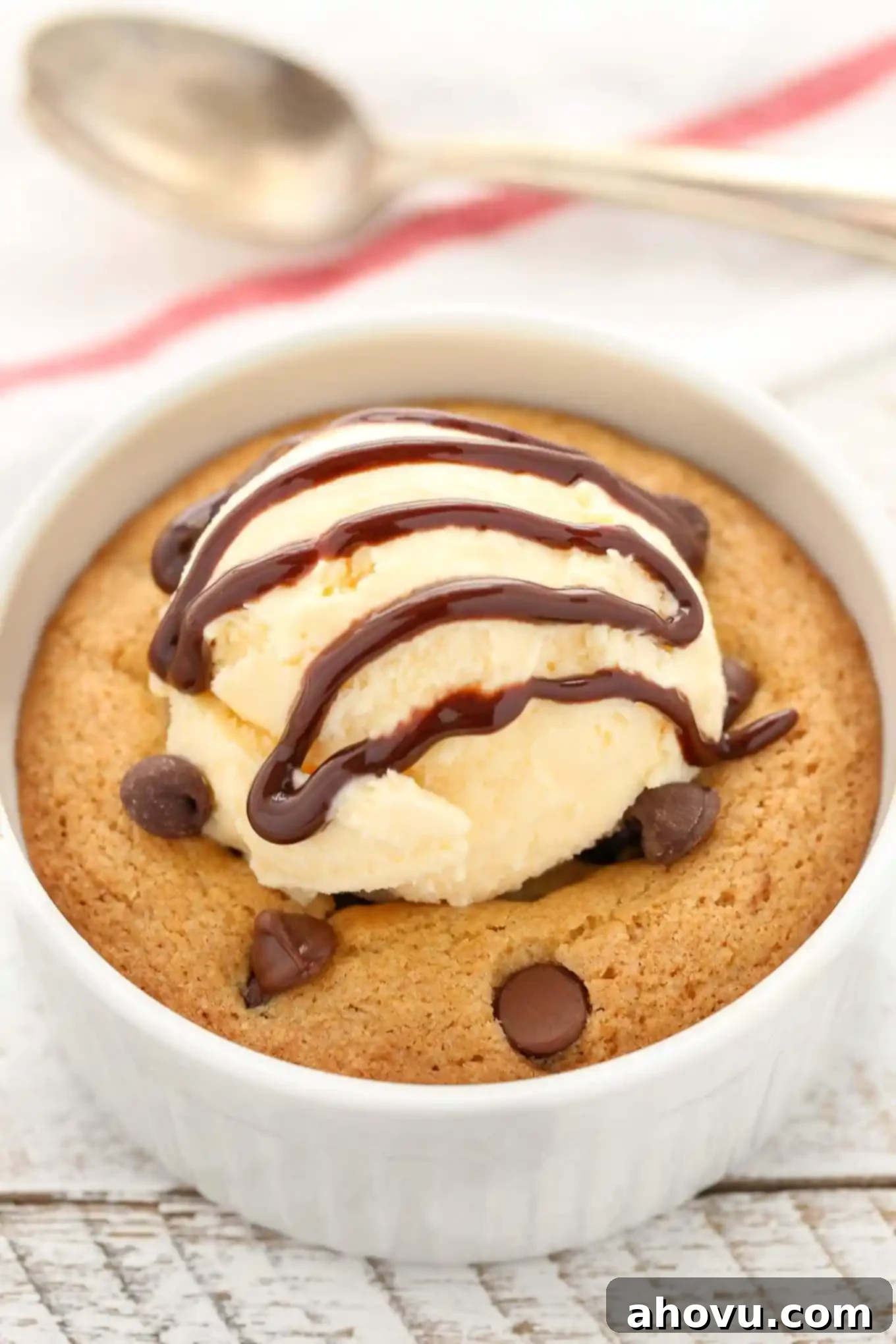 Close up of a deep dish chocolate chip cookie topped with a generous scoop of vanilla ice cream and drizzled with chocolate sauce.