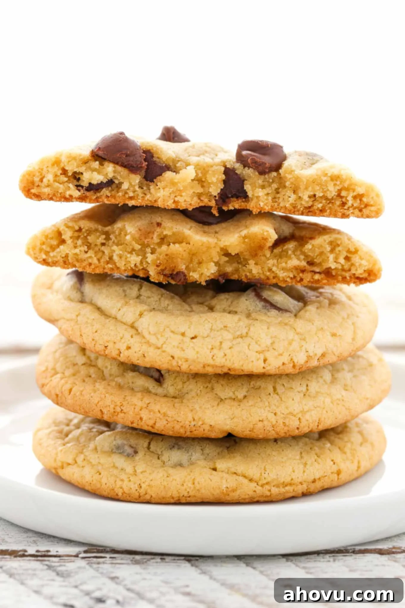 A stack of four thick, soft chocolate chip cookies on a white plate.