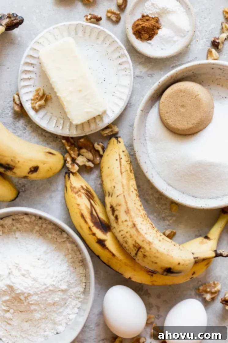 The ingredients needed to make banana bread laying on a gray surface in speckled bowls and plates. This organized display suggests readiness for baking, featuring mashed bananas, butter, sugar, flour, and other essentials.