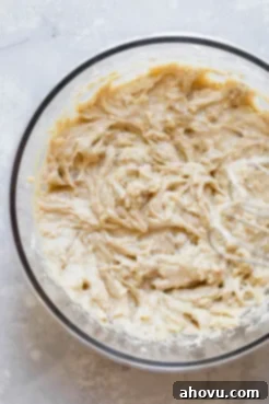 A glass bowl with the finished banana bread batter ready to be poured into a loaf pan. The batter appears thick and well-mixed, indicating proper consistency for baking.