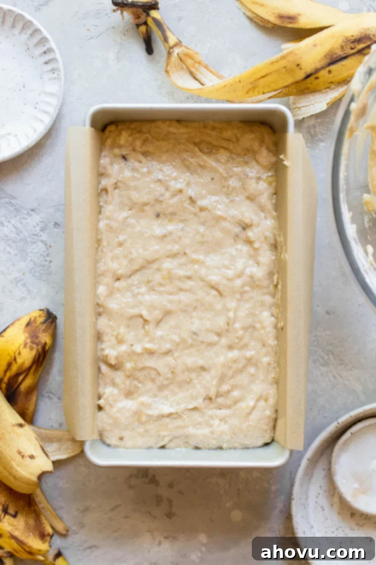 A loaf pan lined with parchment paper holding batter ready to be put into the oven. The batter is smoothed into an even layer, indicating preparation for a uniform bake.