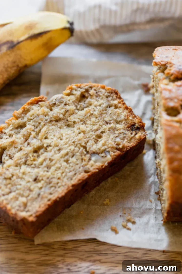 A slice of banana bread cut off the loaf and laying down to show the crust and interior texture of the bread. The golden-brown crust and moist, soft crumb are clearly visible.