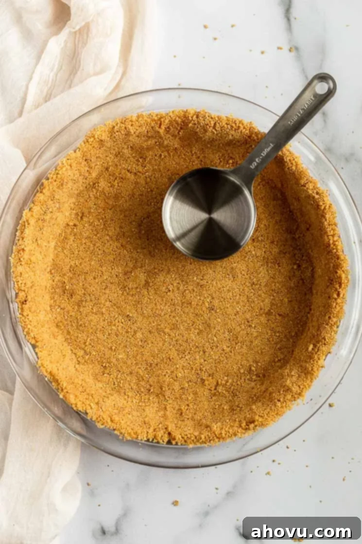 Perfect Homemade Graham Cracker Crust 5 A perfectly pressed graham cracker crust in a pie plate, with a measuring cup beside it, illustrating the pressing technique.