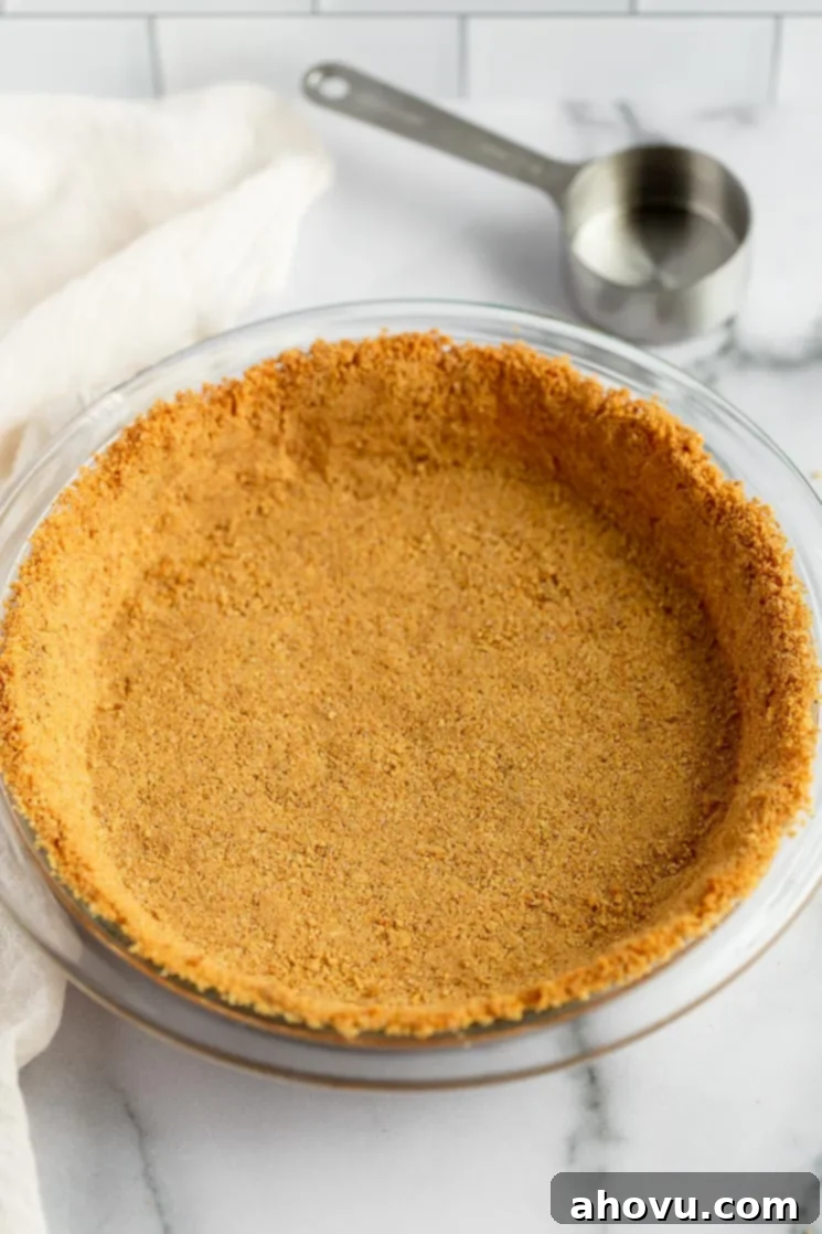 Perfect Homemade Graham Cracker Crust 6 A baked graham cracker crust in a pie plate, cooling with a measuring cup and a cooling rack nearby.