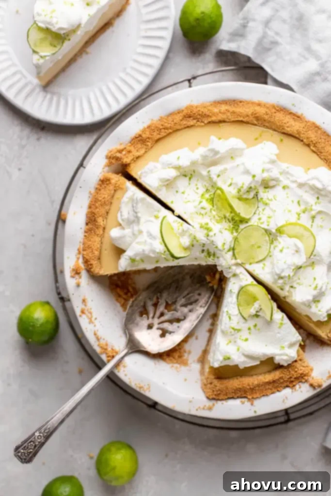 An overhead view of a key lime pie on a white plate, with one slice missing and two more slices cut out. 