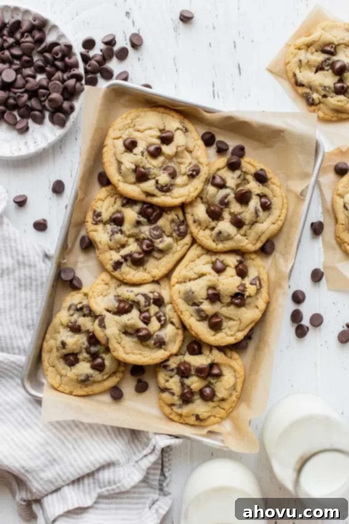 Irresistible Small Batch Chocolate Chip Cookies 2 A pile of chocolate chip cookies on a baking sheet lined with parchment paper surrounded by more cookies and chocolate chips.