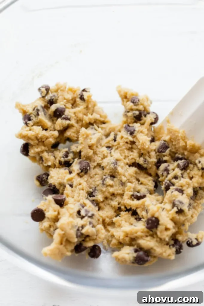 Irresistible Small Batch Chocolate Chip Cookies 4 Cookie batter being mixed together with a white spatula in a clear glass bowl.