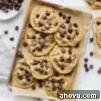 Irresistible Small Batch Chocolate Chip Cookies 7 A pile of chocolate chip cookies on a baking sheet lined with parchment paper surrounded by more cookies and chocolate chips.