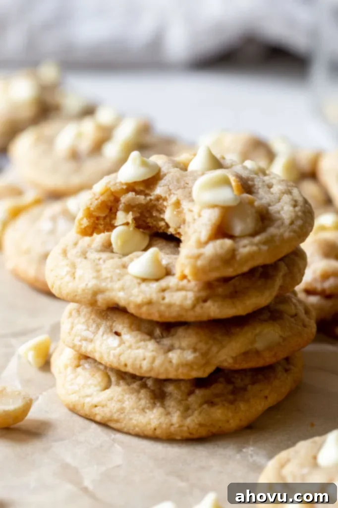 A tantalizing stack of golden-brown white chocolate macadamia nut cookies, surrounded by more freshly baked cookies, showcasing their perfect texture and generous inclusions.