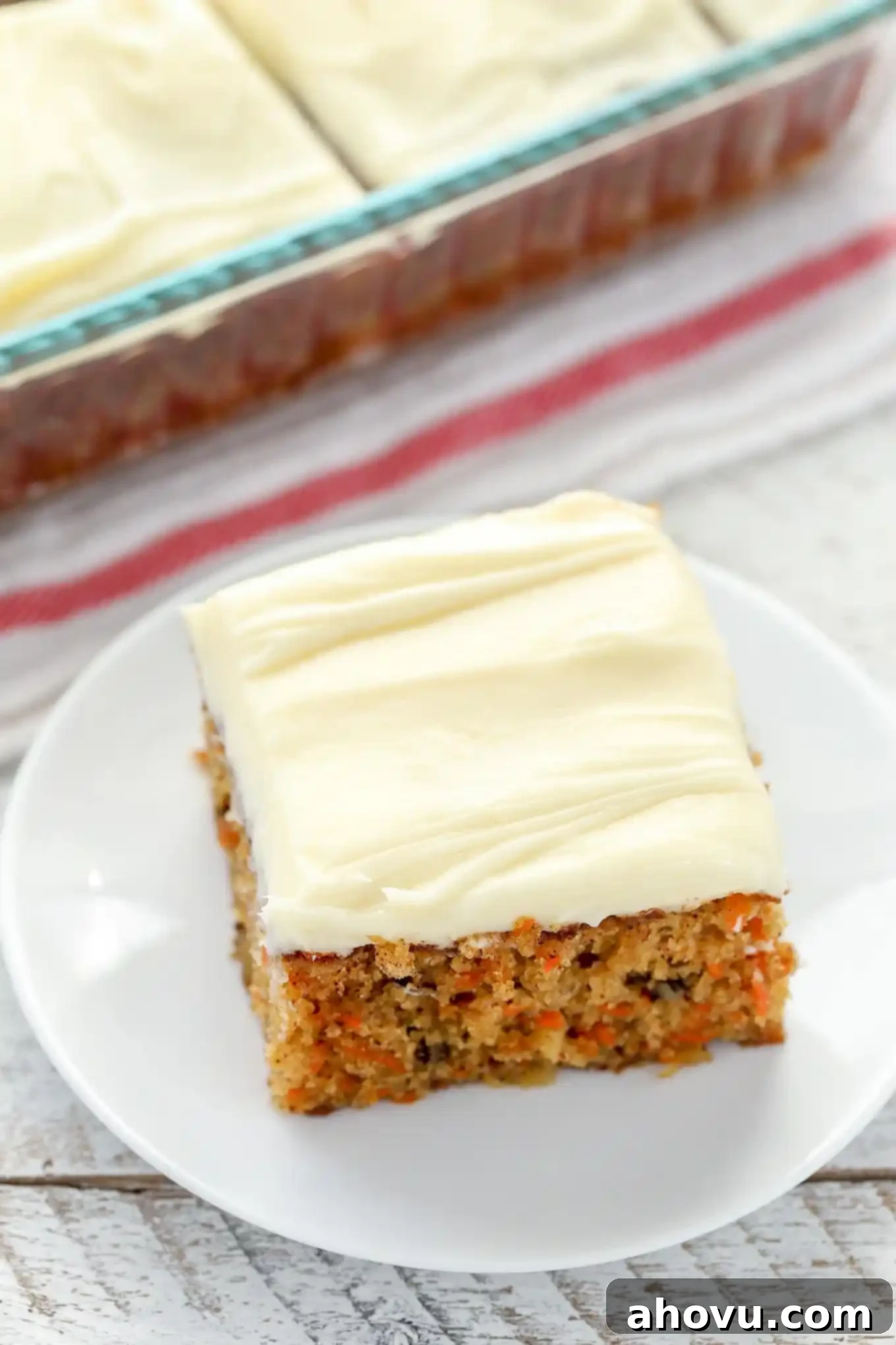 Sun-Kissed Pineapple Carrot Cake 4 A slice of pineapple carrot cake on a white plate, with the rest of the cake in a pan visible in the background.