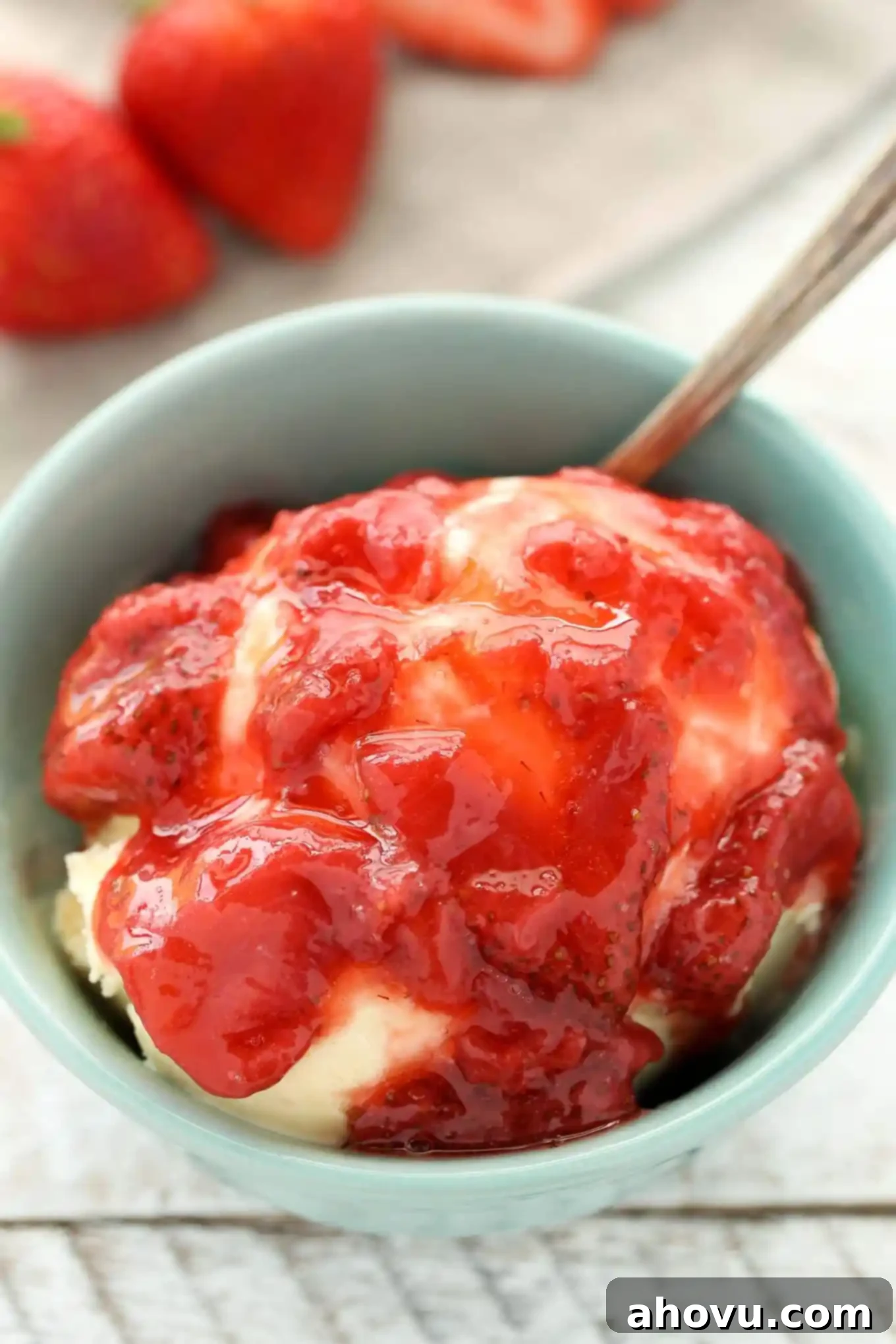 A bowl of ice cream topped with strawberry sauce. Fresh berries are lined up in the background. 