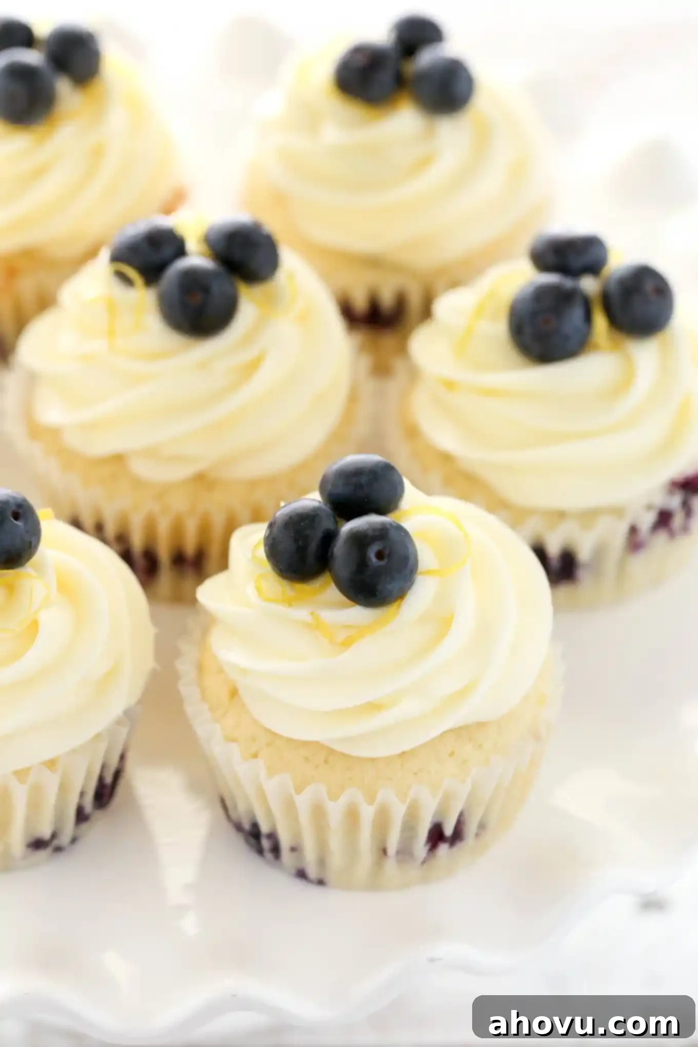 Overhead shot of freshly baked lemon blueberry cupcakes adorned with piped lemon cream cheese frosting and a scattering of fresh blueberries.