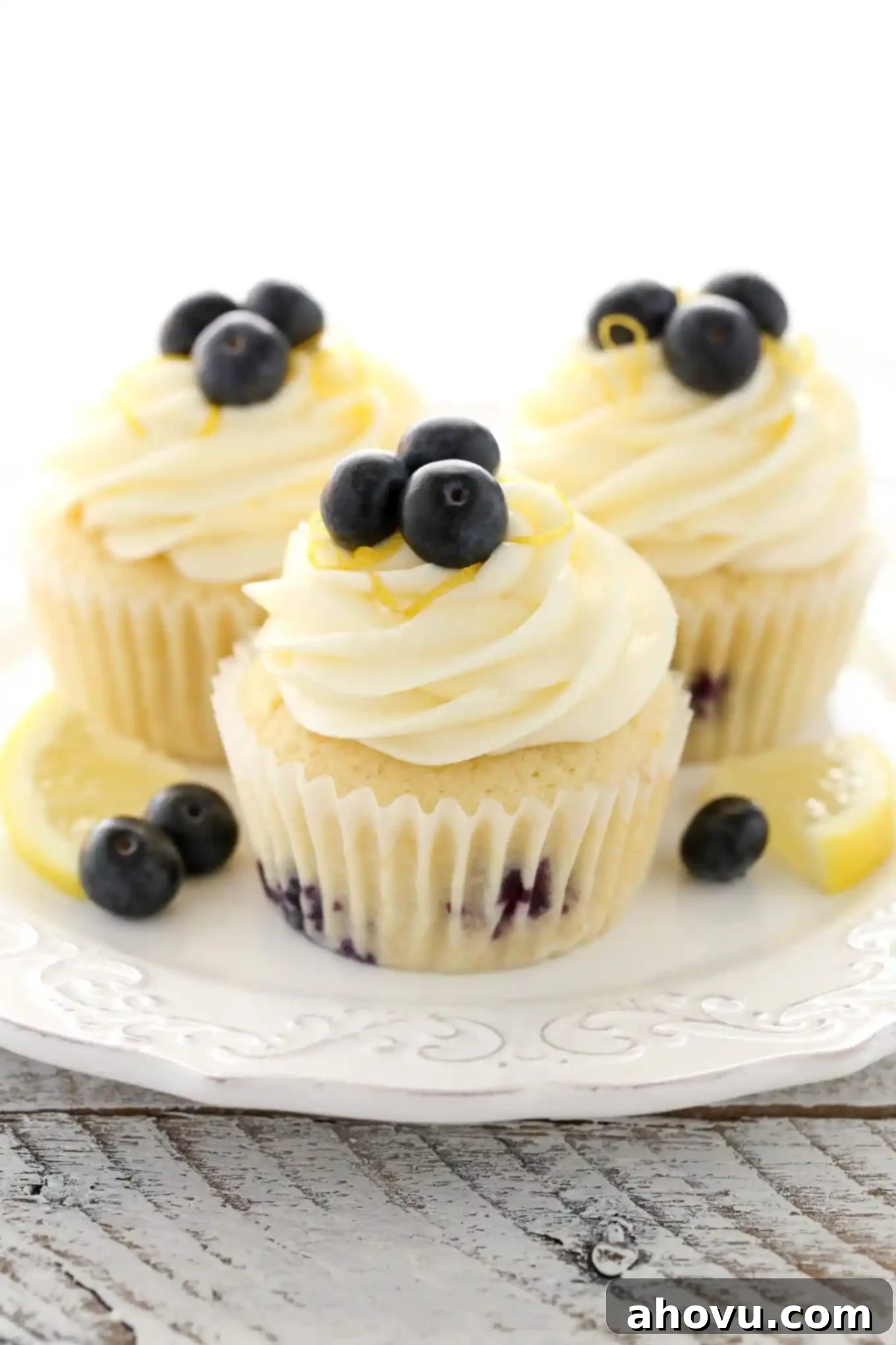 Three perfectly frosted lemon blueberry cupcakes presented elegantly on a pristine white dessert plate.