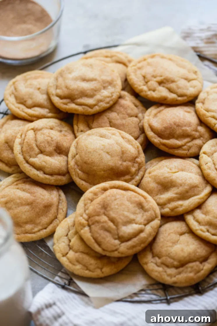 Ultimate Soft and Chewy Snickerdoodles 6 An antique round cooling rack holding a pile of perfectly baked snickerdoodle cookies, with a glass of milk and a bowl of cinnamon sugar nearby.