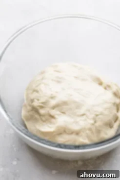 A glass mixing bowl holding the finished dough that needs to rise, smooth and ready for fermentation, essential for soft cinnamon rolls.