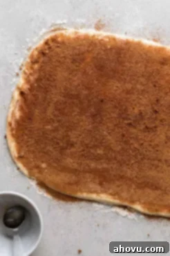 Cinnamon roll dough rolled out into a rectangle and generously topped with softened butter, rich brown sugar, and aromatic cinnamon, ready for rolling to form perfect swirls.