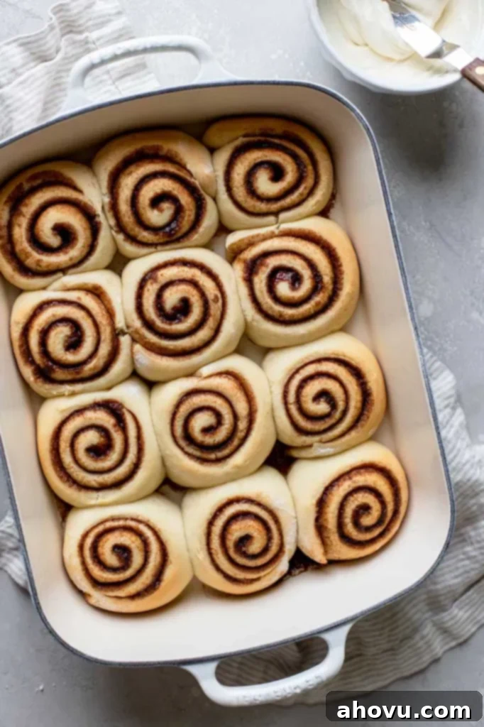 A white baking pan holding freshly baked cinnamon rolls that are cooling before being topped with a delicious, creamy icing.