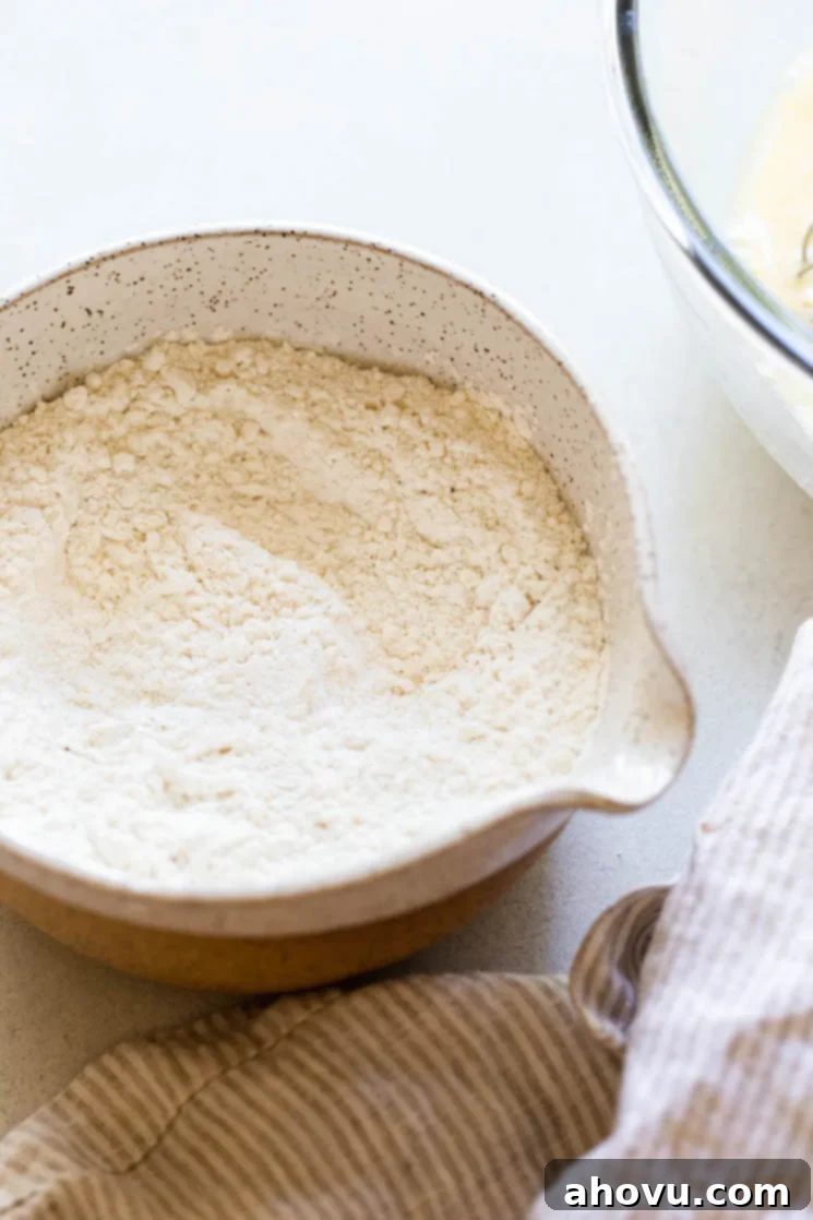 The perfectly measured dry ingredients for buttermilk pancakes, including all-purpose flour, baking powder, baking soda, and salt, mixed together in a white speckled clay bowl, ready for the wet ingredients.