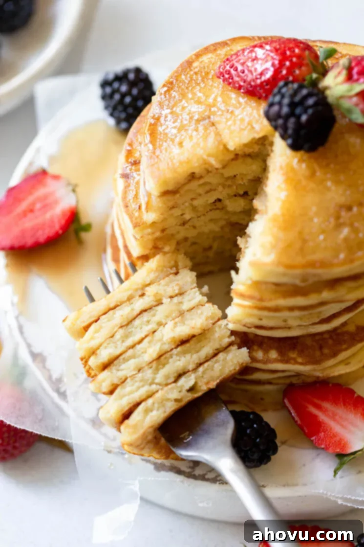 A beautifully composed stack of fluffy buttermilk pancakes adorned with fresh berries and a generous pour of maple syrup, with a fork holding a perfect bite-sized piece cut from the stack.