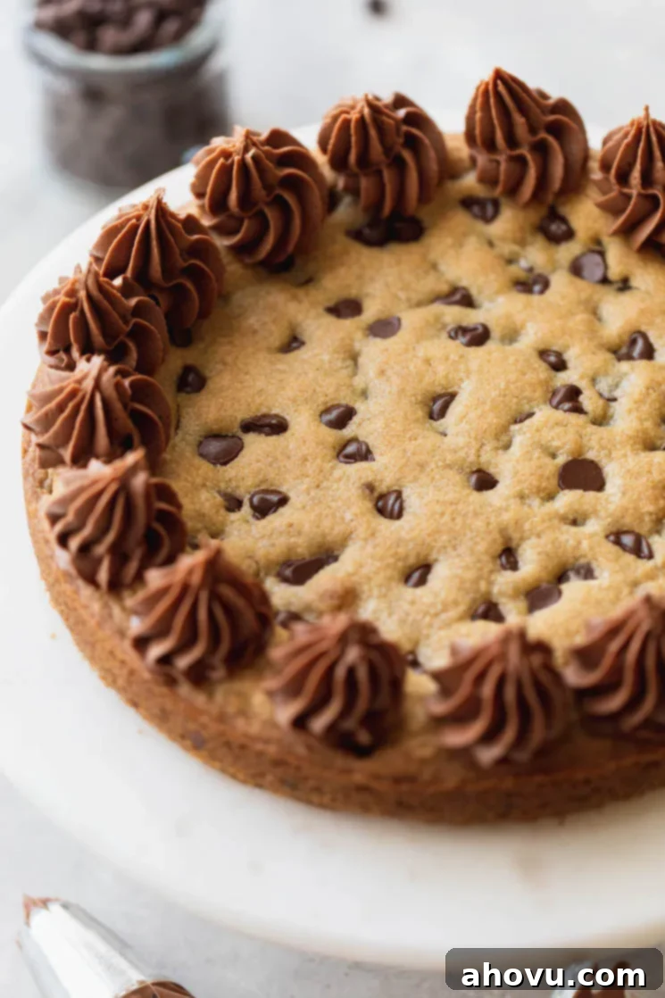 A finished chocolate chip cookie cake, beautifully decorated with chocolate buttercream frosting, displayed on a elegant marble cake stand. Perfect for a birthday or special occasion.