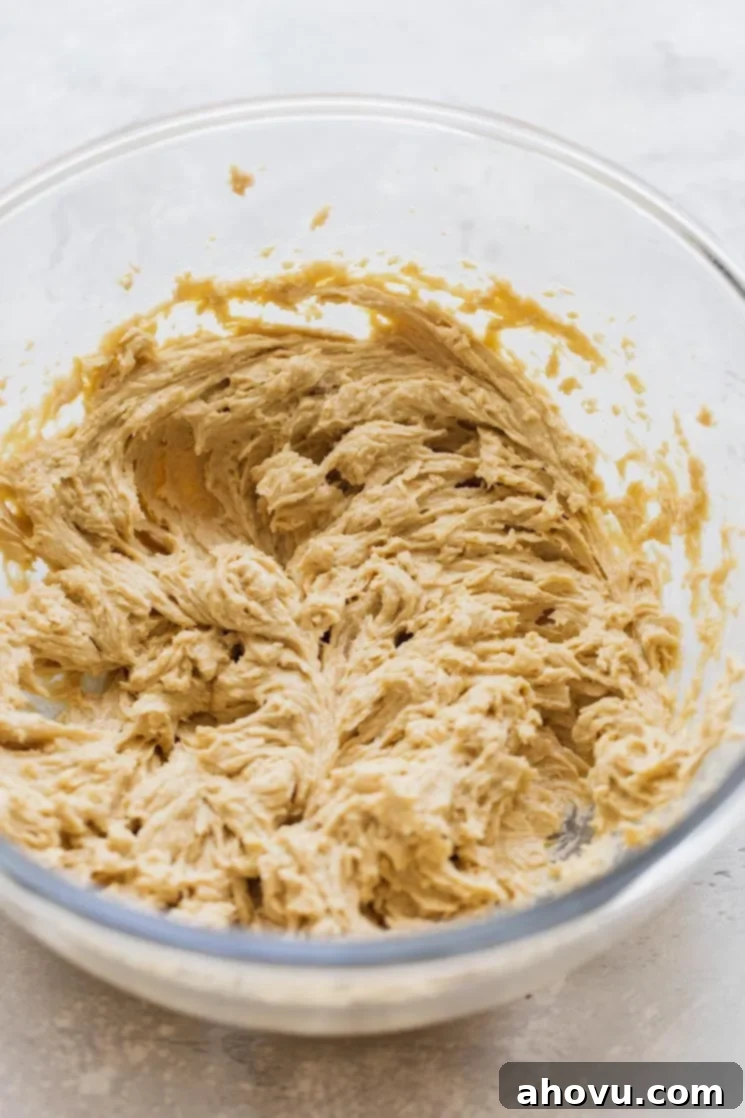 A glass mixing bowl filled with the wet ingredients – butter, sugar, egg, and vanilla – for making the chocolate chip cookie cake batter.