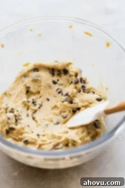 A glass mixing bowl holding finished chocolate chip cookie cake batter ready to be put in the baking pan.
