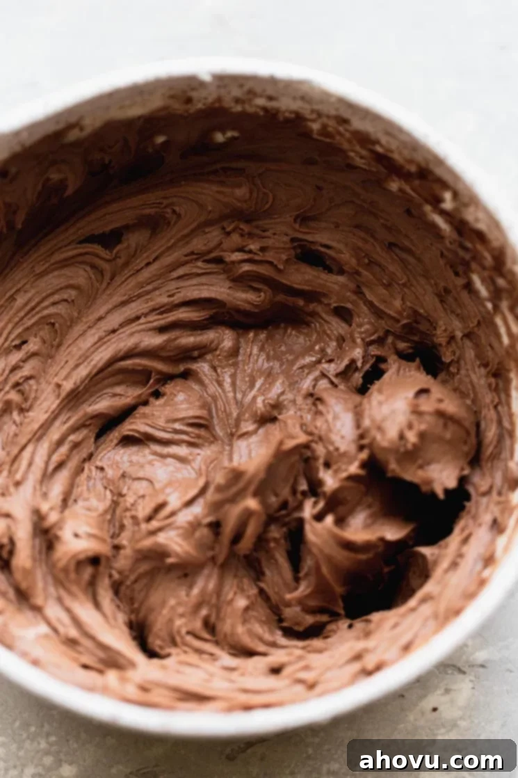 A white mixing bowl filled with homemade chocolate buttercream frosting, ready to be piped onto the cooled cookie cake.