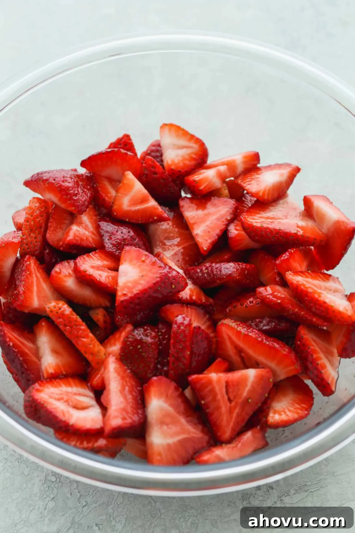 A sparkling clean glass bowl filled with vibrant, freshly sliced strawberries, ready to be macerated for the shortcake.
