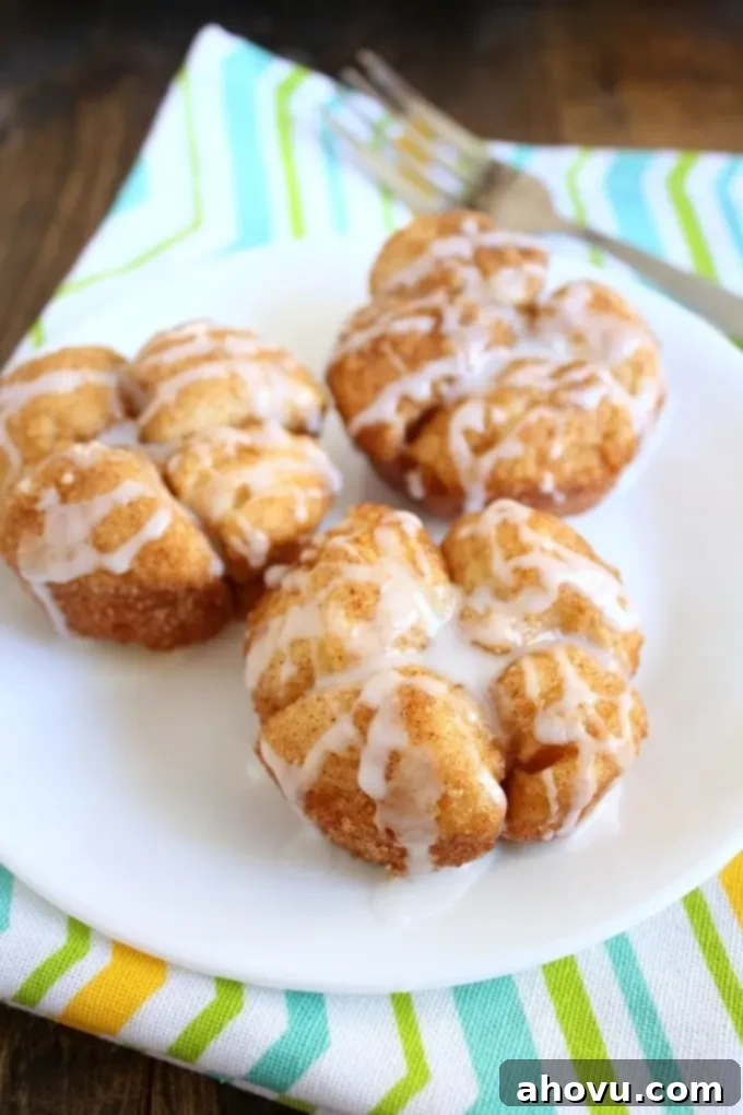 Three Monkey Bread Muffins on a white plate. A fork and striped napkin rest near the plate. 