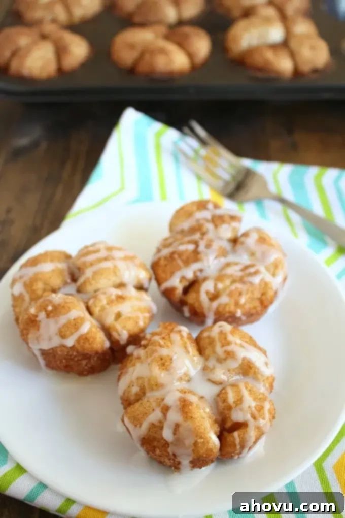 Three pull apart Monkey Bread Muffins on a white plate. A pan of muffins rests in the background. 