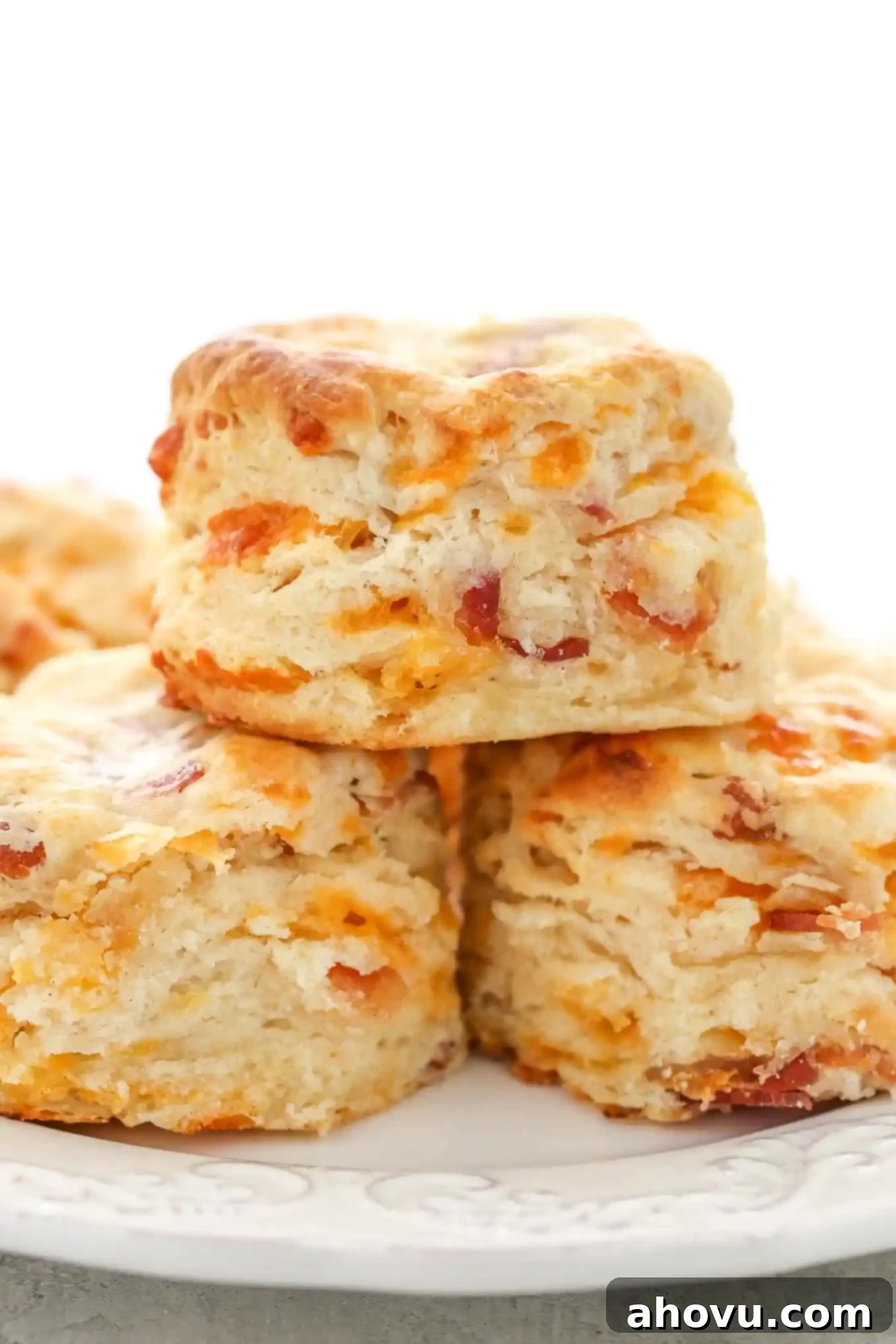 A stack of three golden-brown bacon cheese biscuits on a white plate, showing their fluffy texture.