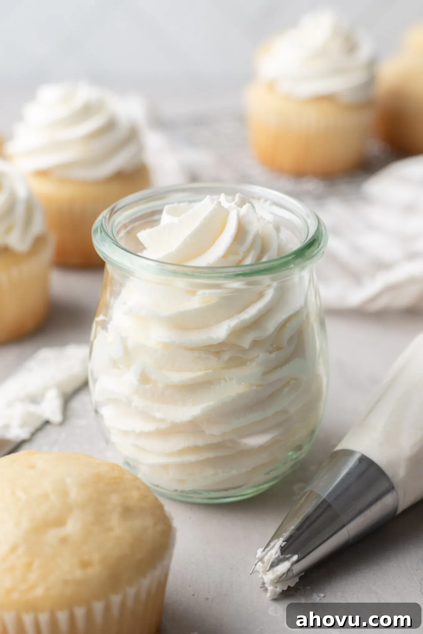 A glass jar filled with whipped cream. Vanilla cupcakes surround the jar. 