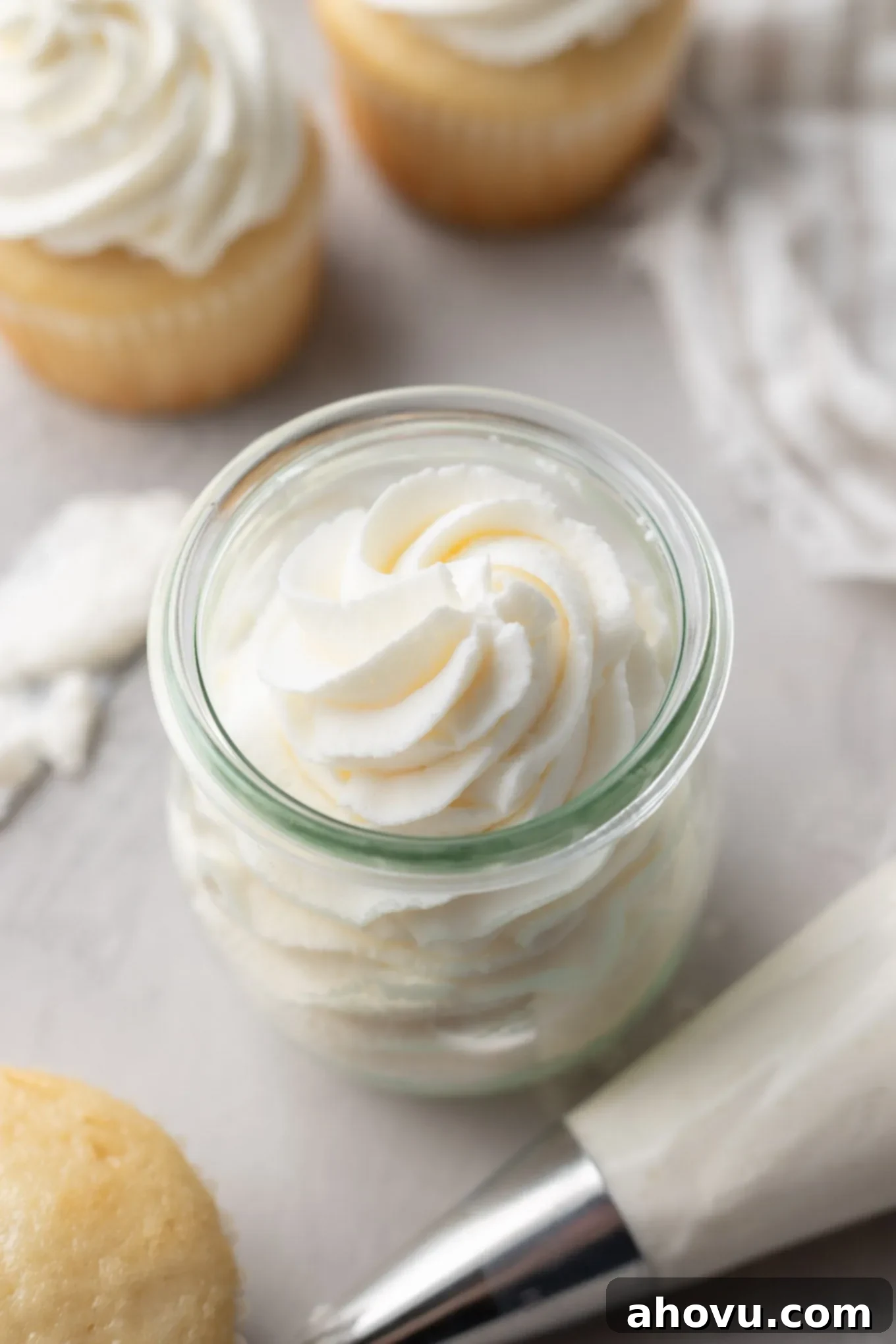 An overhead view of stabilized whipped cream in a glass jar, next to vanilla cupcakes. 