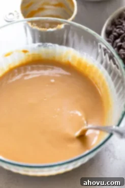 Peanut butter and melted butter whisked together in a large glass bowl. A spoon rests inside the bowl.