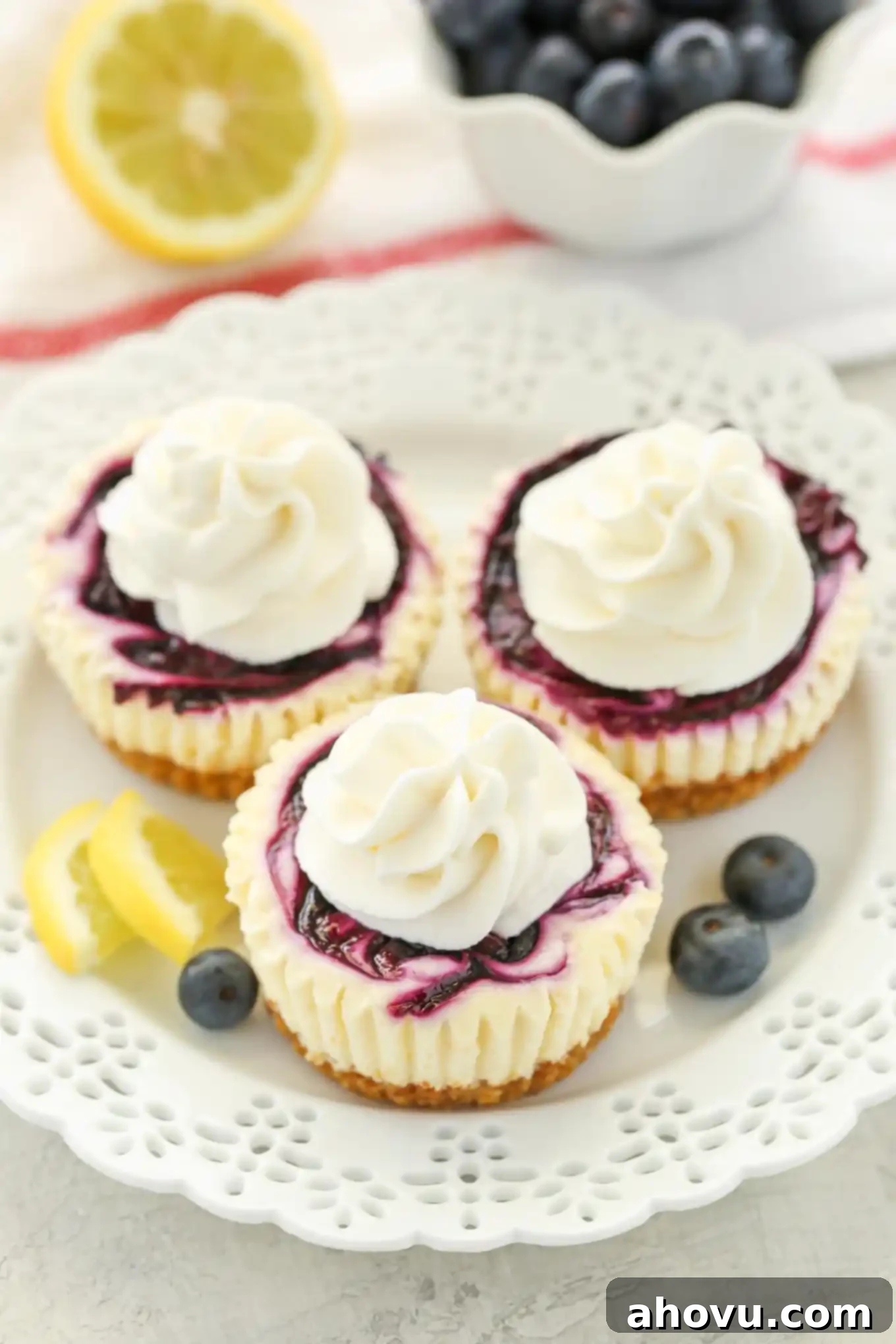 Lemon Blueberry Cheesecake Bites 2 Three mini lemon blueberry cheesecake bites topped with whipped cream on a white plate.