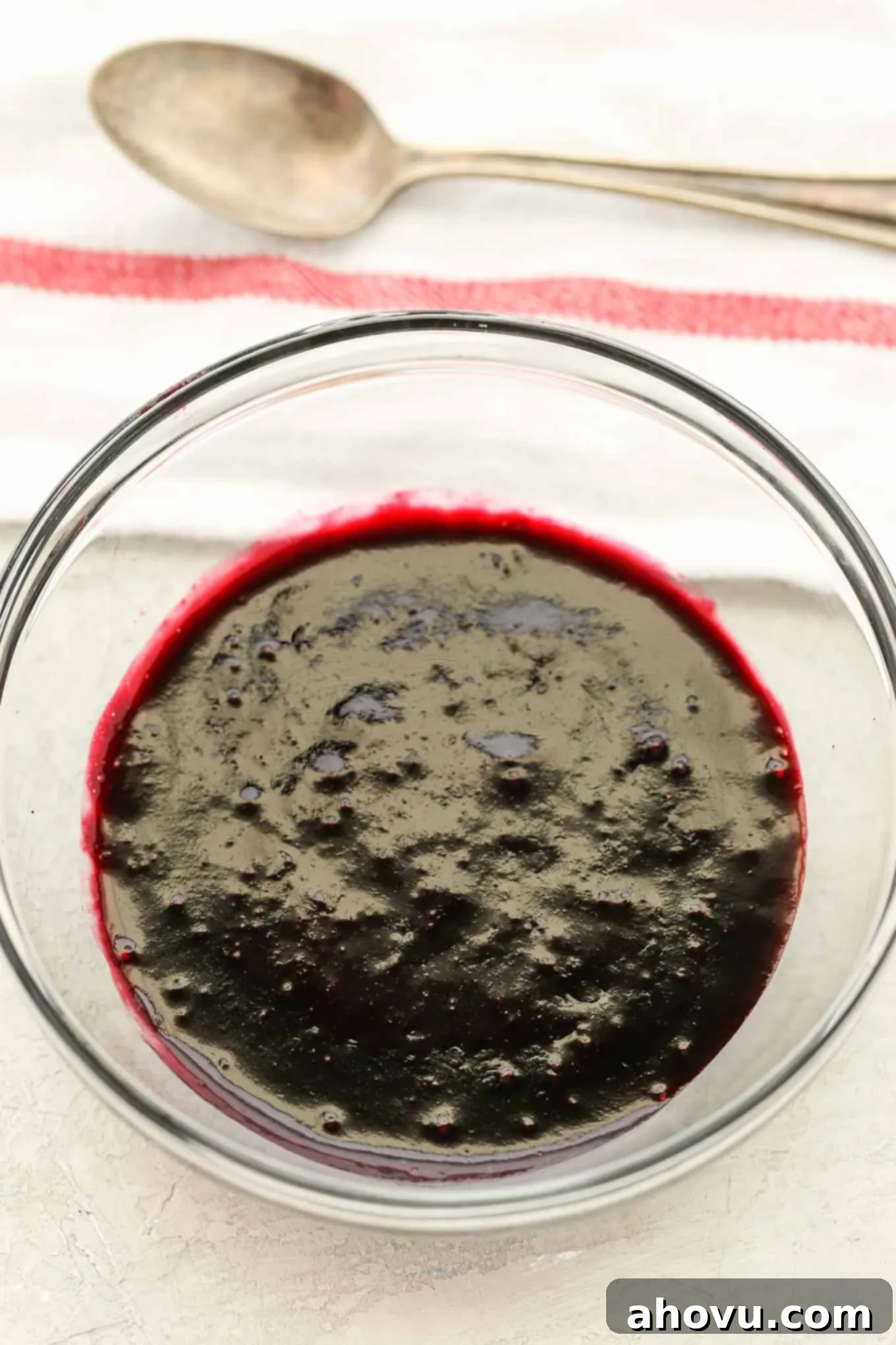 Lemon Blueberry Cheesecake Bites 4 Blueberry sauce for cheesecake in a glass bowl. A spoon and striped towel are behind it.