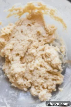 A close-up of biscuit topping dough, perfectly mixed with small pea-sized butter crumbs, resting in a clear glass bowl, ready to be scooped onto the cobbler.