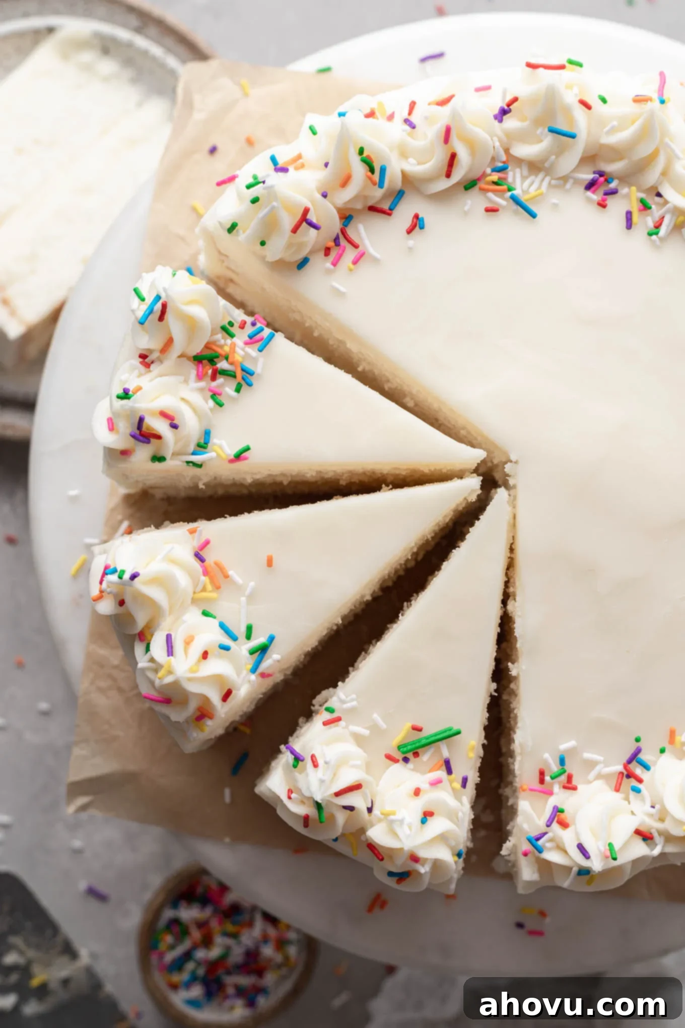 An overhead view of a homemade white cake on a cake stand. Three slices have been cut. 
