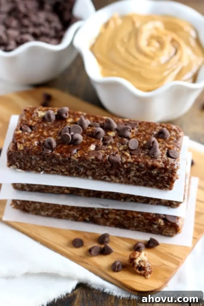 Effortless No-Bake Chocolate Peanut Butter Granola Bars 2 A stack of three peanut butter chocolate chip granola bars on pieces of parchment paper. A bowl of chocolate chips and a bowl of peanut butter rest in the background.